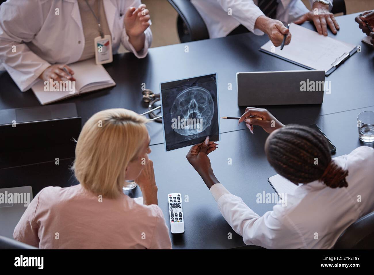 Prise de vue à angle élevé d'une femme afro-américaine tenant une image tomodensitométrique du crâne du patient discutant des résultats de l'examen radiographique avec un collègue, tout en étant assis à TAB Banque D'Images