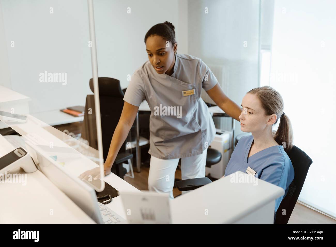 Médecin féminin parlant avec une infirmière assise sur une chaise au bureau à l'hôpital Banque D'Images