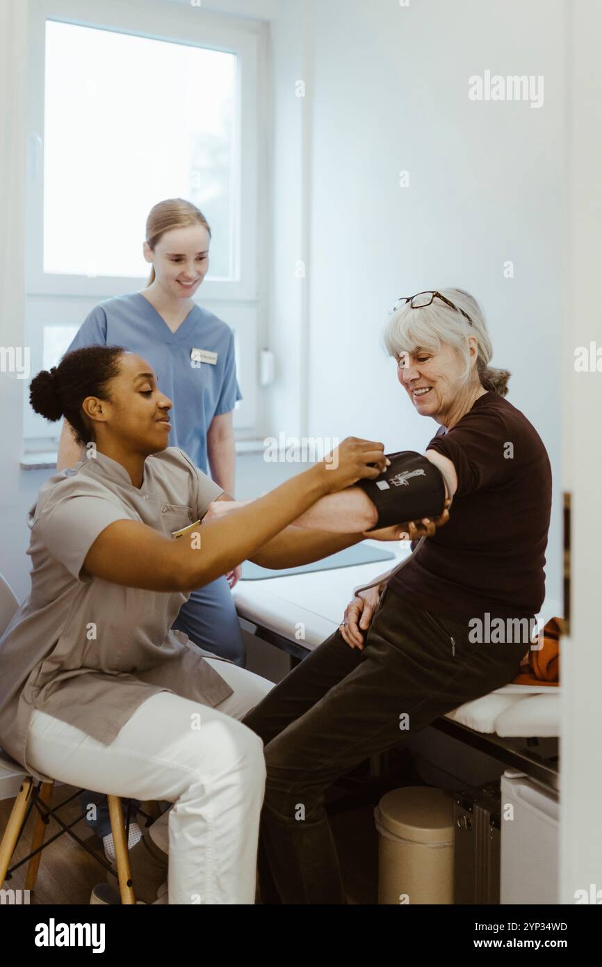 Médecin féminin vérifiant la pression artérielle d'une femme âgée assise dans la salle d'examen Banque D'Images
