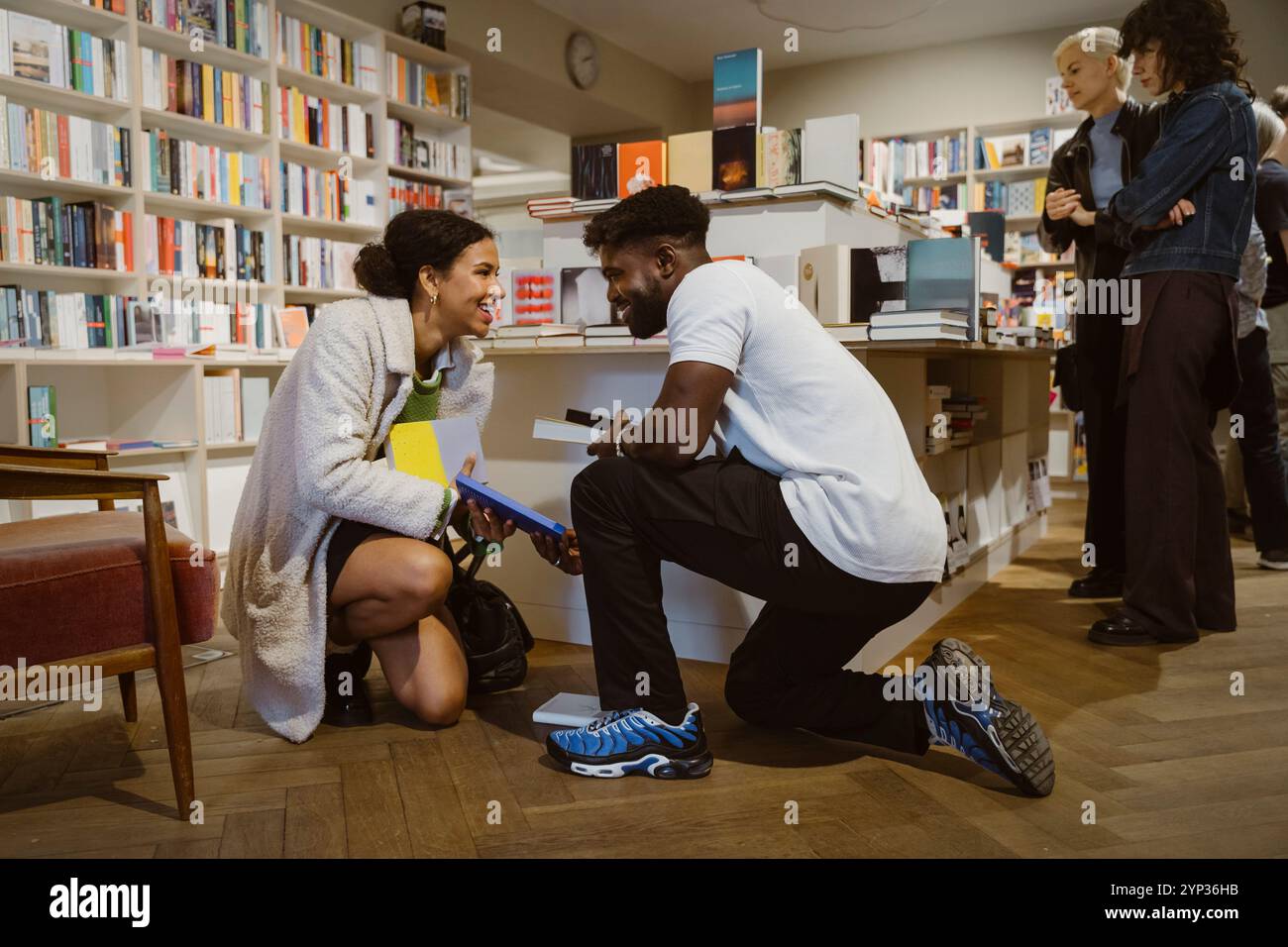Homme et femme souriants se regardant tout en ramassant des livres à la boutique Banque D'Images