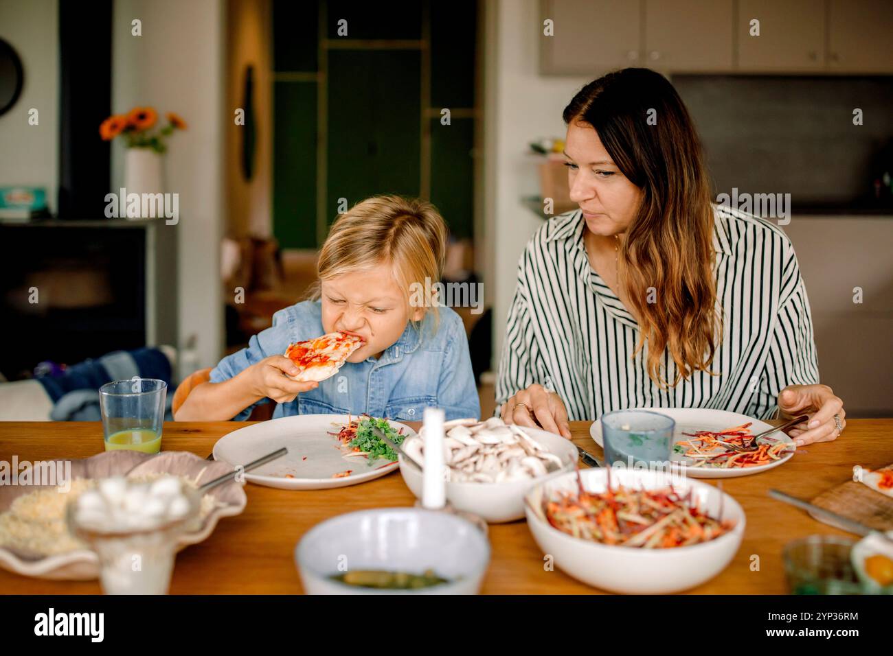 Garçon mangeant de la pizza tout en étant assis à côté de la mère à la table à manger à la maison Banque D'Images