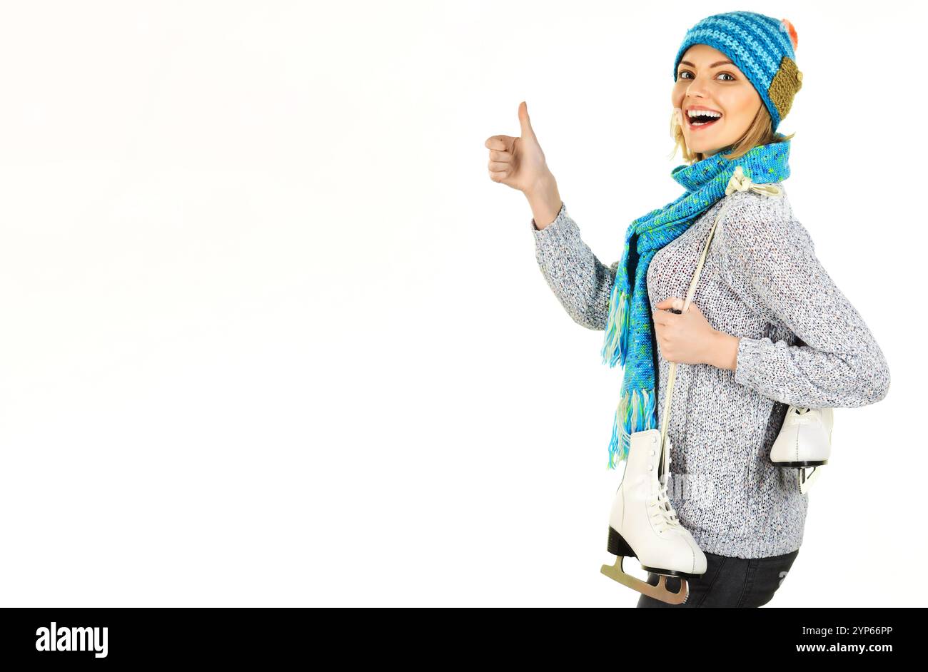 Femme heureuse dans des vêtements d'hiver avec des patins à glace montrant le pouce vers le haut. Sports d'hiver. Patin à glace fille. Femme sportive en pull chaud, chapeau et écharpe avec patin Banque D'Images