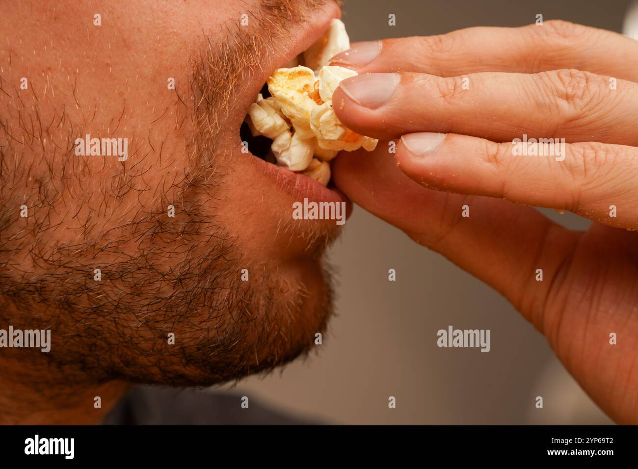 Un gros plan d'un homme tenant du pop-corn dans ses mains, soulignant le moment de plaisir du repas. Parfait pour un concept lié à la nourriture et relaxati Banque D'Images