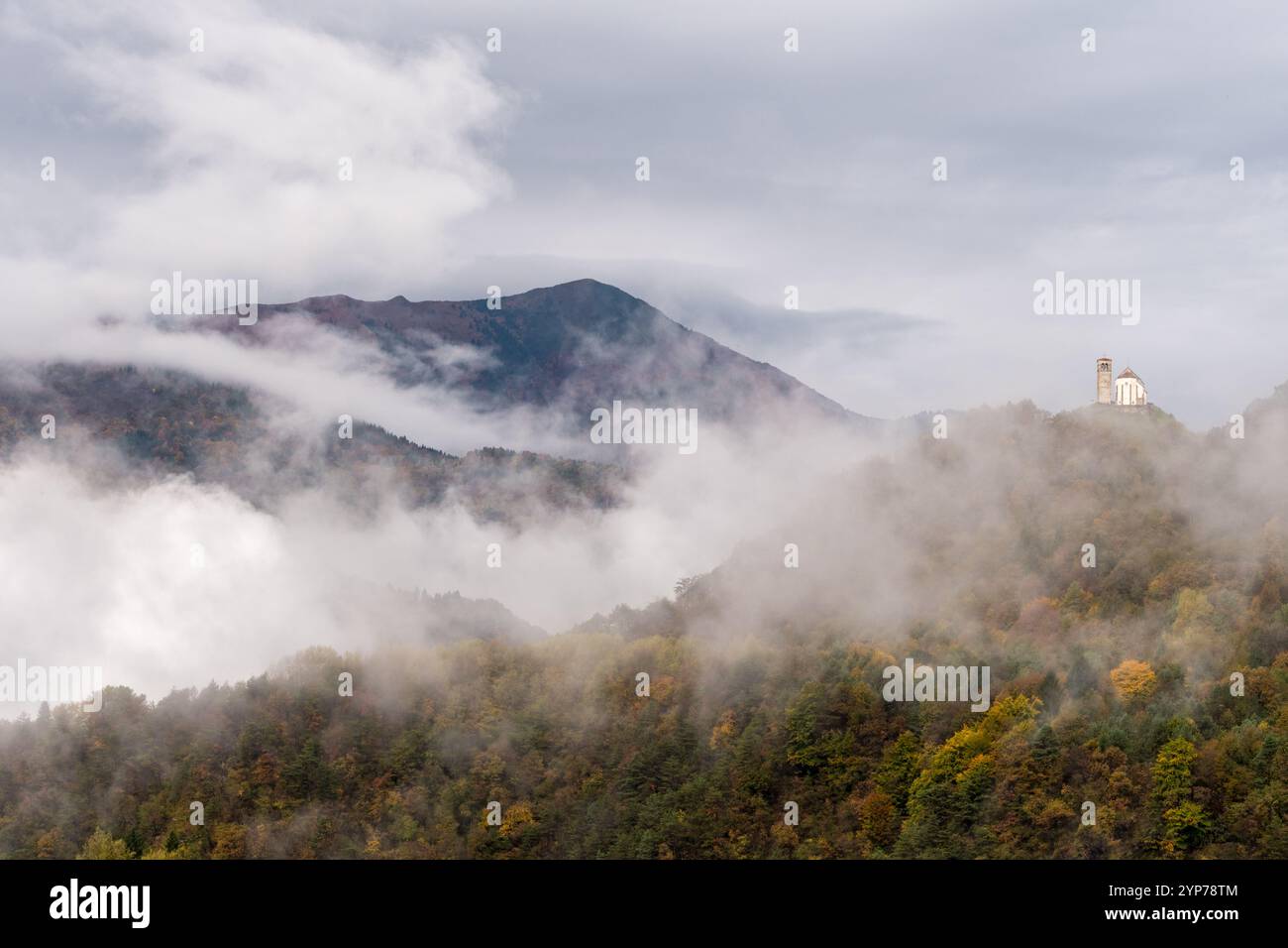 Paysage de montagne suggestif avec brouillard et rayons de soleil. Ancienne église solitaire sur le sommet de la montagne, couleurs d'automne. Banque D'Images