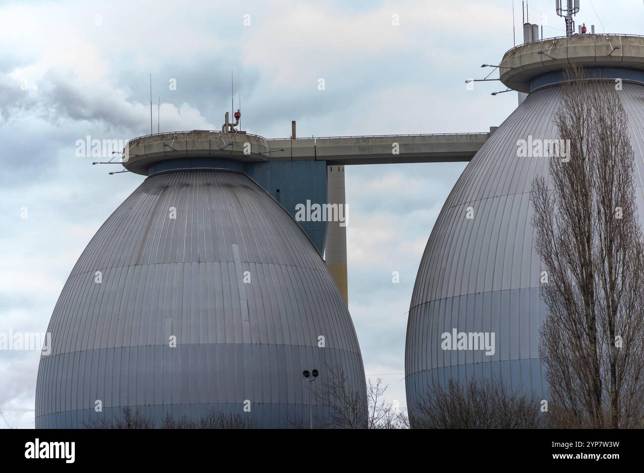 Deux grands réservoirs industriels reliés par une passerelle, sous un ciel gris Banque D'Images