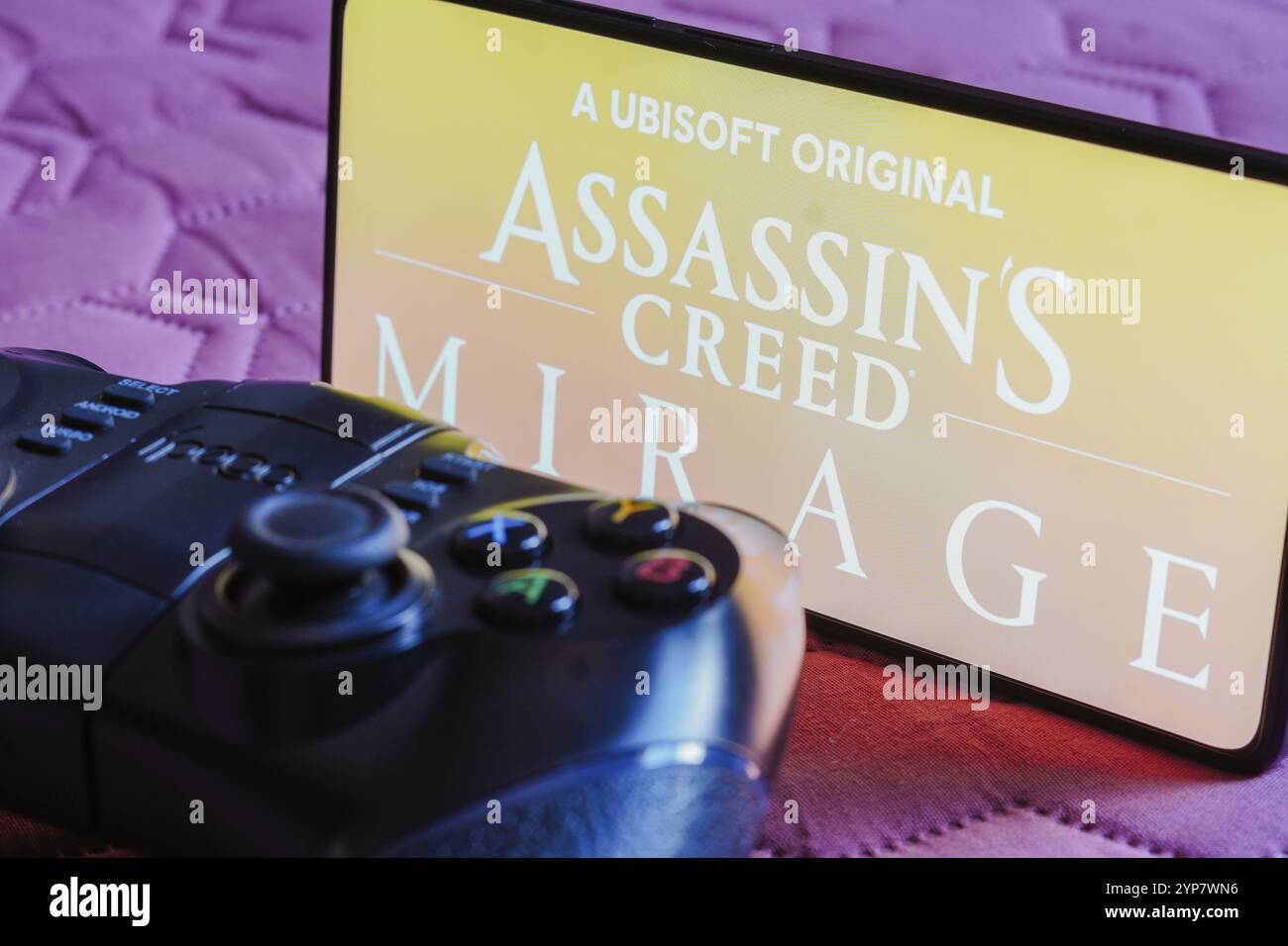Dans cette illustration photo, le logo Assassin's Creed Mirage est affiché sur l'écran d'un smartphone, à côté d'une manette de jeu Banque D'Images