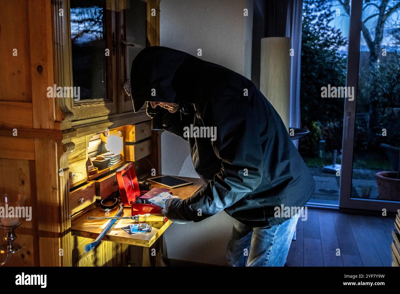 Image symbolique d'un cambriolage, l'auteur est entré par effraction dans un appartement du côté du jardin et est à la recherche de butin, ouvre une caisse, trouve val Banque D'Images