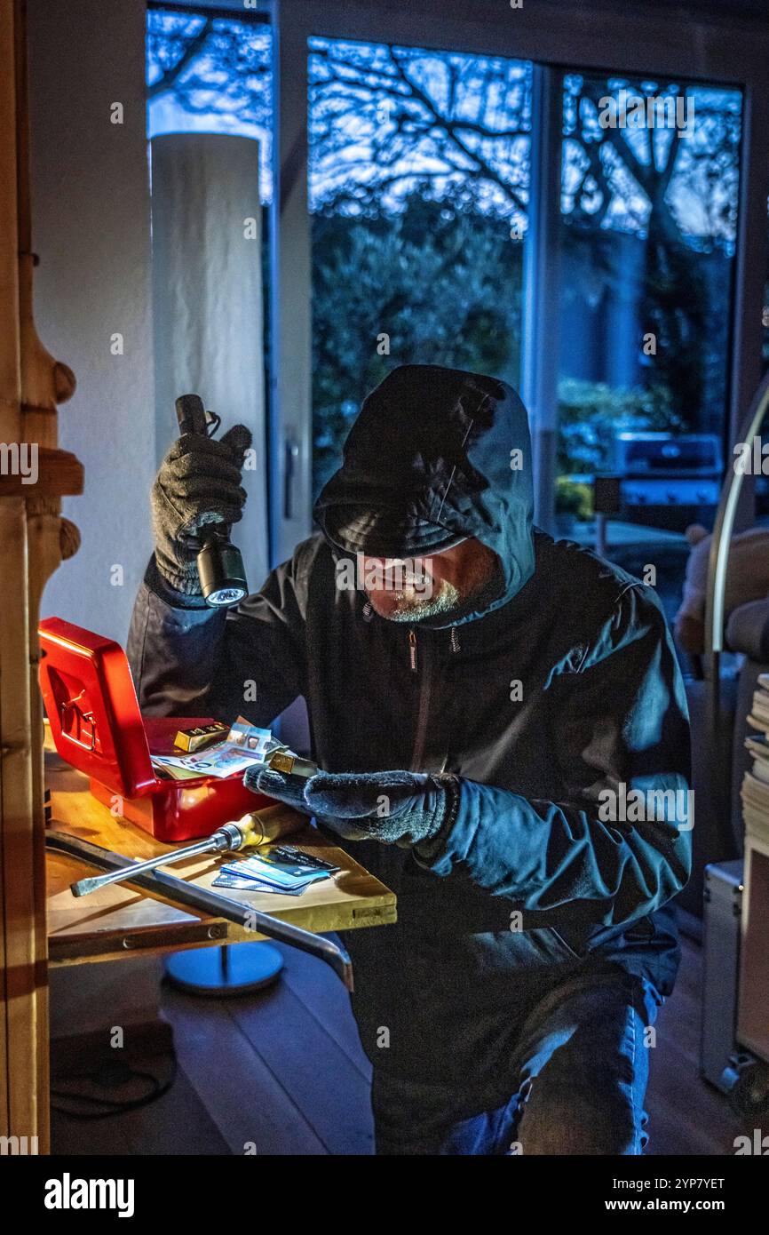 Image symbolique d'un cambriolage, l'auteur est entré par effraction dans un appartement du côté du jardin et est à la recherche de butin, ouvre une caisse, trouve val Banque D'Images