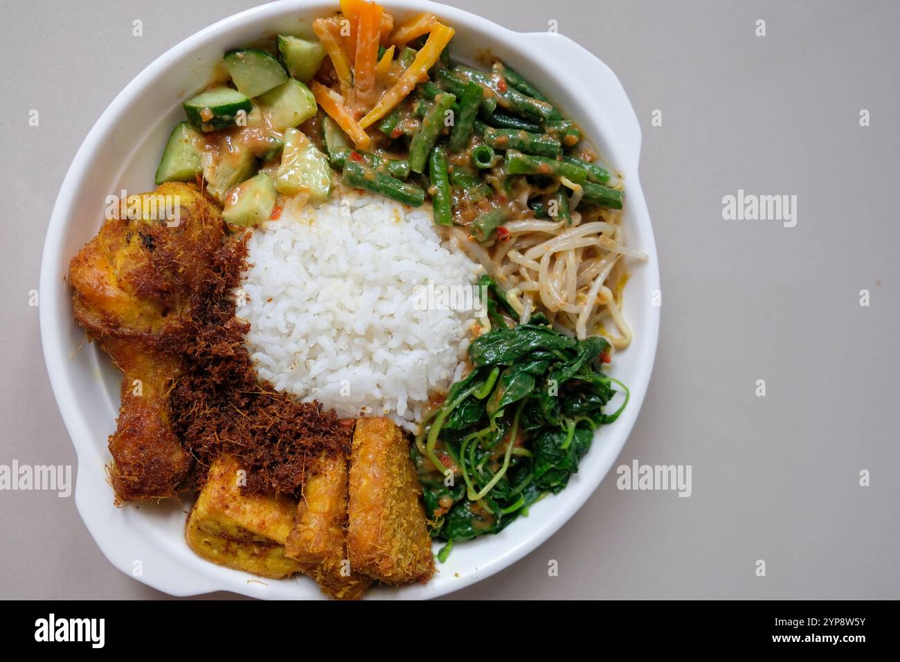 Une nourriture maison indonésienne, riz avec pecel, tempeh, tofu et ayam goreng lengkuas ou poulet frit au galanga dans une assiette. Vue de dessus, espace de copie. Banque D'Images
