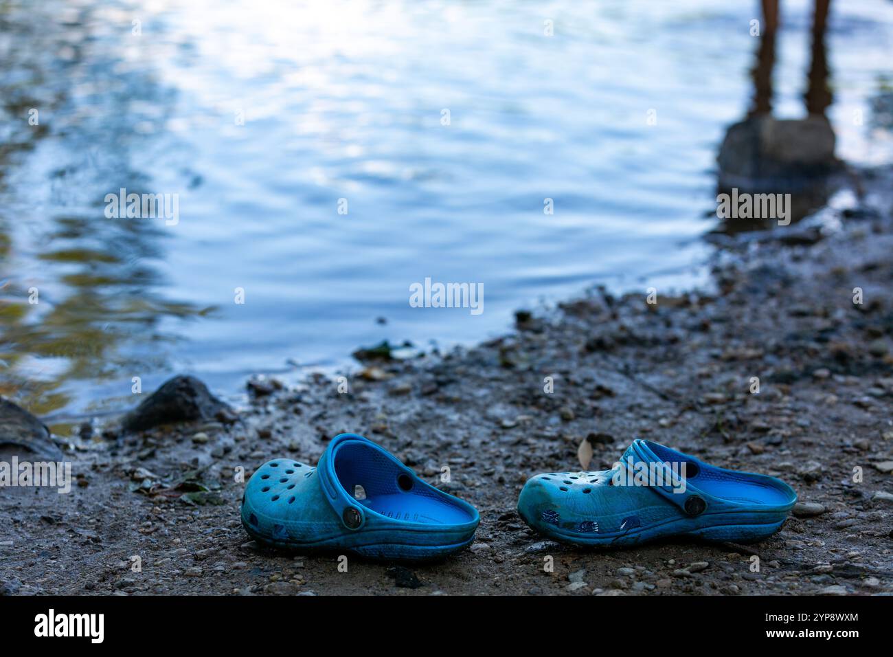 Une paire de sabots Crocs bleus se trouve sur la plage à côté du bord de l'eau au lac Sand dans le parc d'État de Chain O' Lakes près d'Albion, Indiana, États-Unis. Banque D'Images