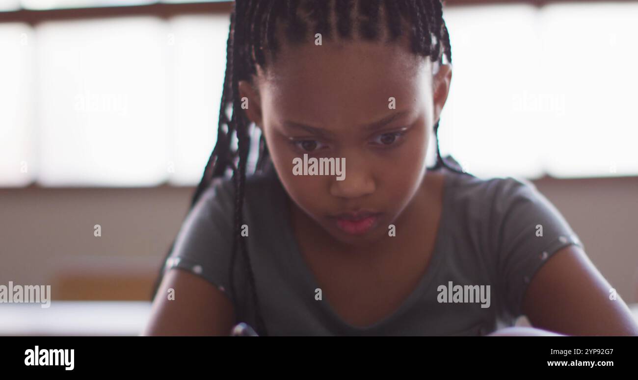 Fille biraciale dessinant une ligne alors qu'elle était assise sur son bureau à l'école Banque D'Images