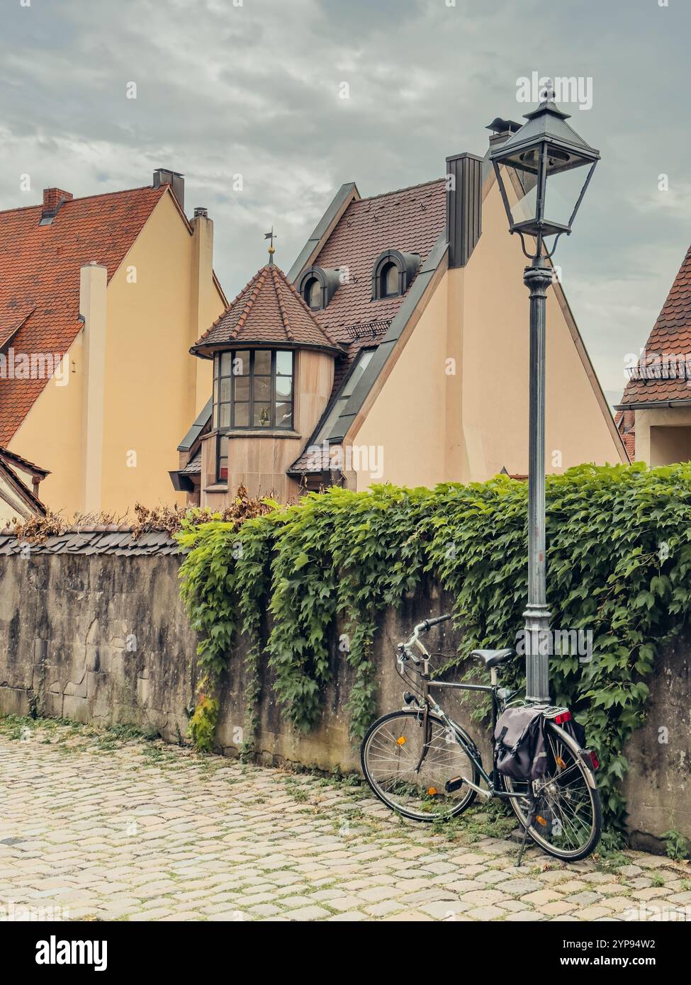 Vélo noir sous un buisson près d'une clôture en pierre près d'une vieille maison avec un toit de tuiles rouges dans la vieille ville de Nuremberg Banque D'Images