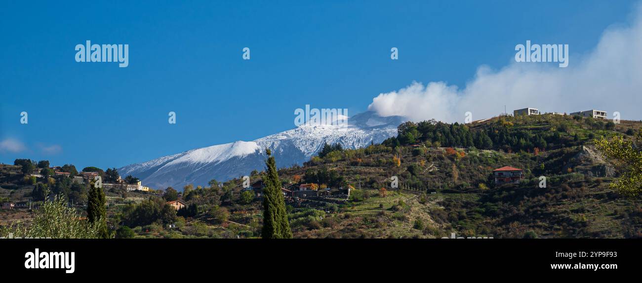 Paysage d'hiver panoramique montrant l'Etna avec la neige et la vapeur de l'activité volcanique, vu de Bronte colline avec des maisons rurales typiques et moi Banque D'Images