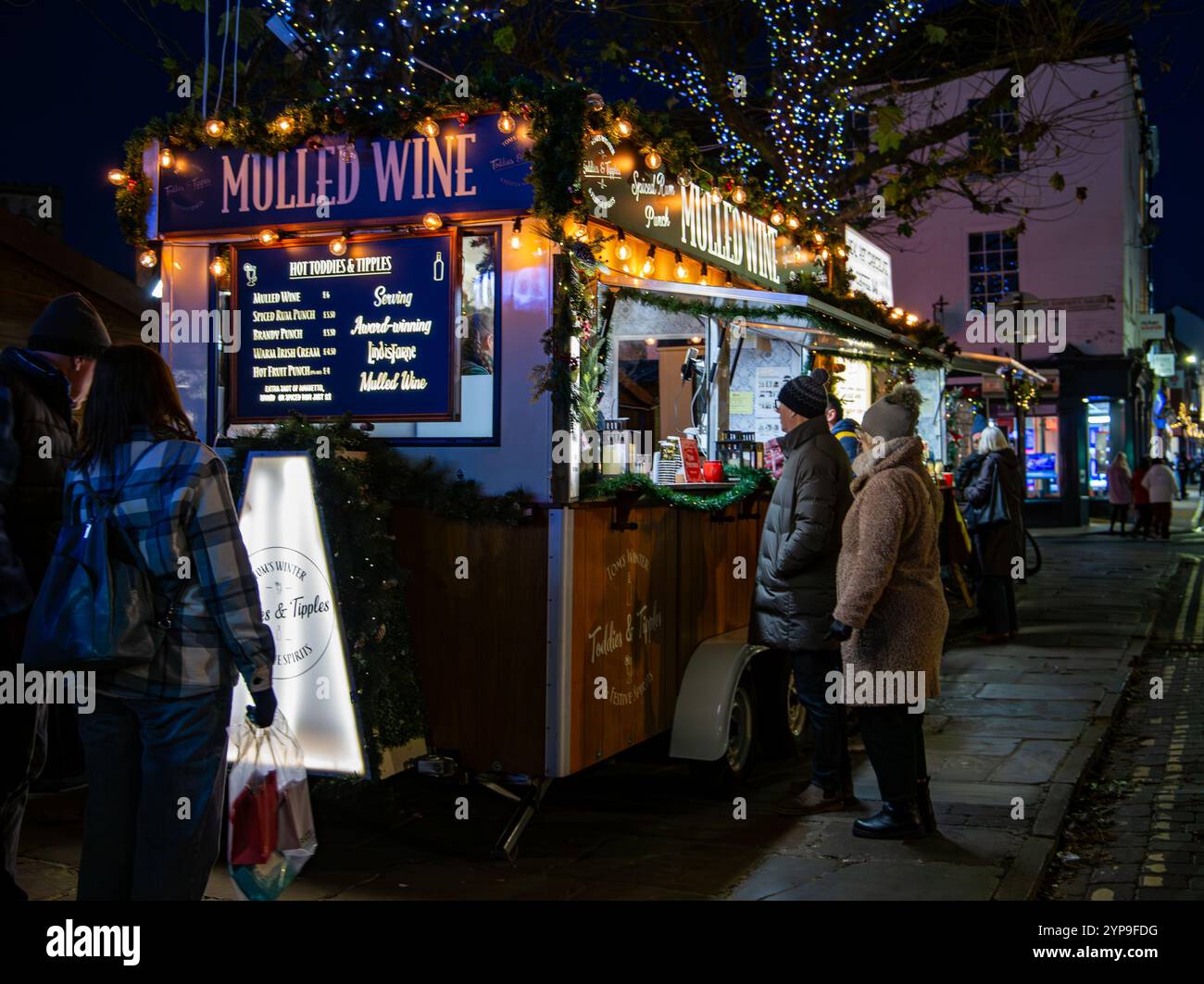Une scène de marché d'hiver festif avec des gens se réunissant à un étal de vin chaud orné de lumières de Noël et de décorations York Christmas Market 2024 Banque D'Images
