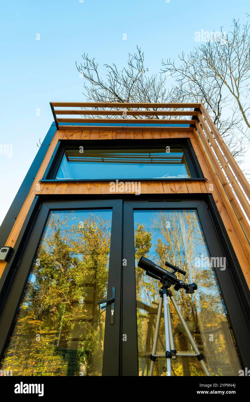 Une petite maison en bois (Homnest) avec de grandes fenêtres et une porte noire se dresse sur une pelouse herbeuse avec des arbres en arrière-plan. Puy de Dome. Auvergne. France Banque D'Images