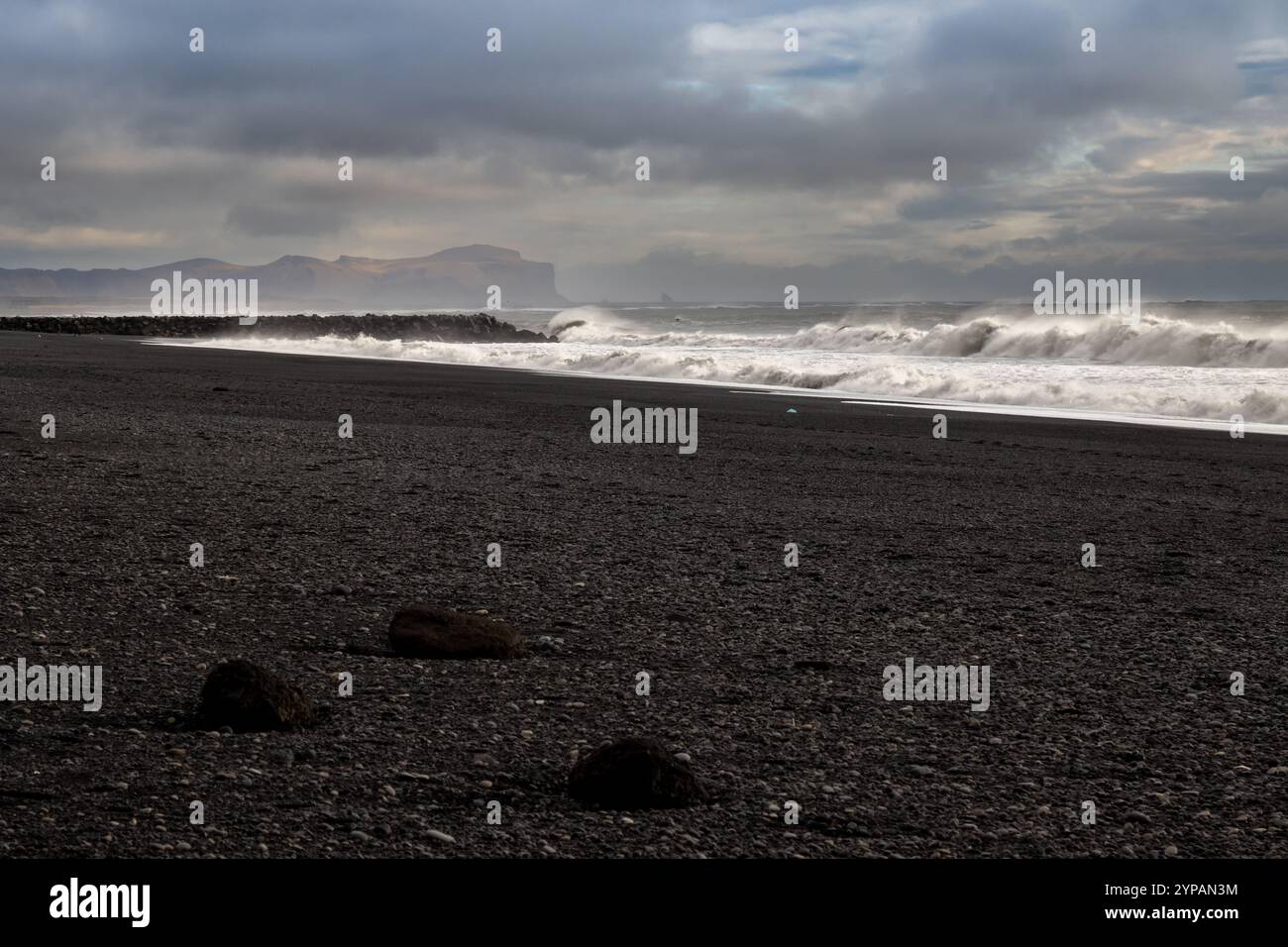 Grandes vagues de l'océan Atlantique sur la plage de sable volcanique noir, créant un contraste à couper le souffle. Montagne en arrière-plan. Ciel nuageux. Vikurfjara, Banque D'Images