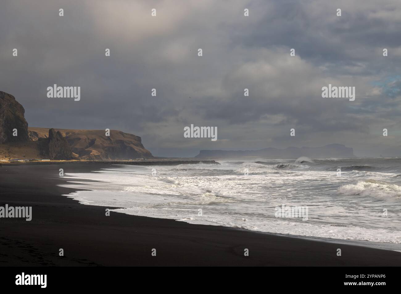 Grandes vagues de l'océan Atlantique sur la plage de sable volcanique noir, créant un contraste à couper le souffle. Montagne en arrière-plan. Ciel nuageux. Vikurfjara, Banque D'Images
