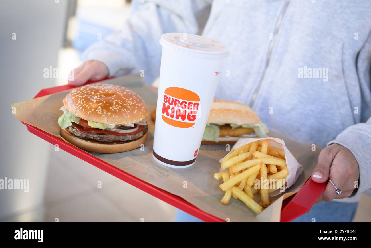 Hanovre, Allemagne. 29 novembre 2024. ILLUSTRATION - Une femme porte un plateau de hamburgers à base de plantes Whopper et long Chicken et des pépites à base de plantes ainsi que des frites et du Coca dans un restaurant de la chaîne de restauration rapide Burger King. Crédit : Julian Stratenschulte/dpa/Alamy Live News Banque D'Images