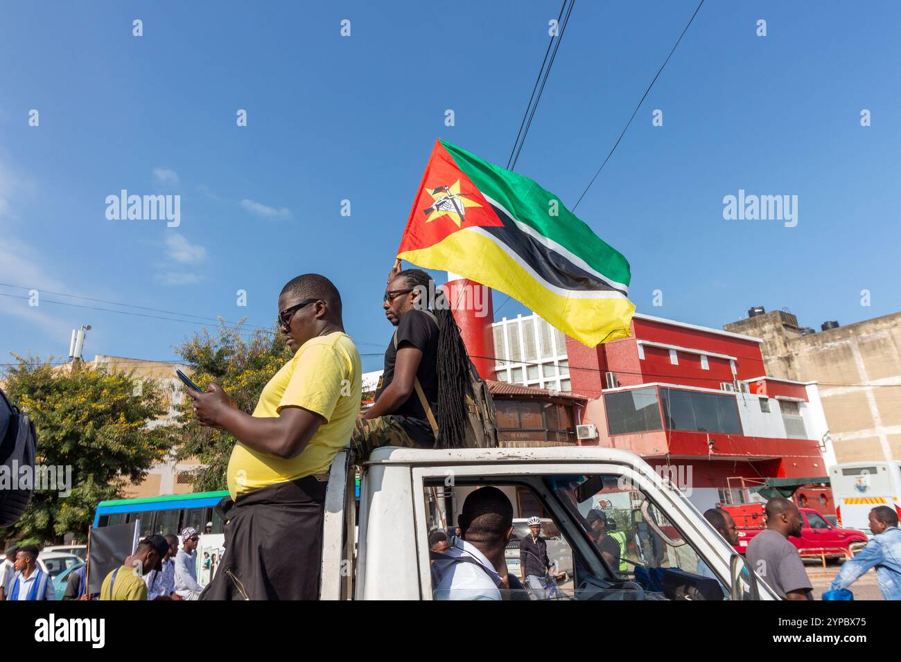 Un homme se repose dans son lit pendant qu'un camion passe, portant fièrement et agitant le drapeau du Mozambique Banque D'Images