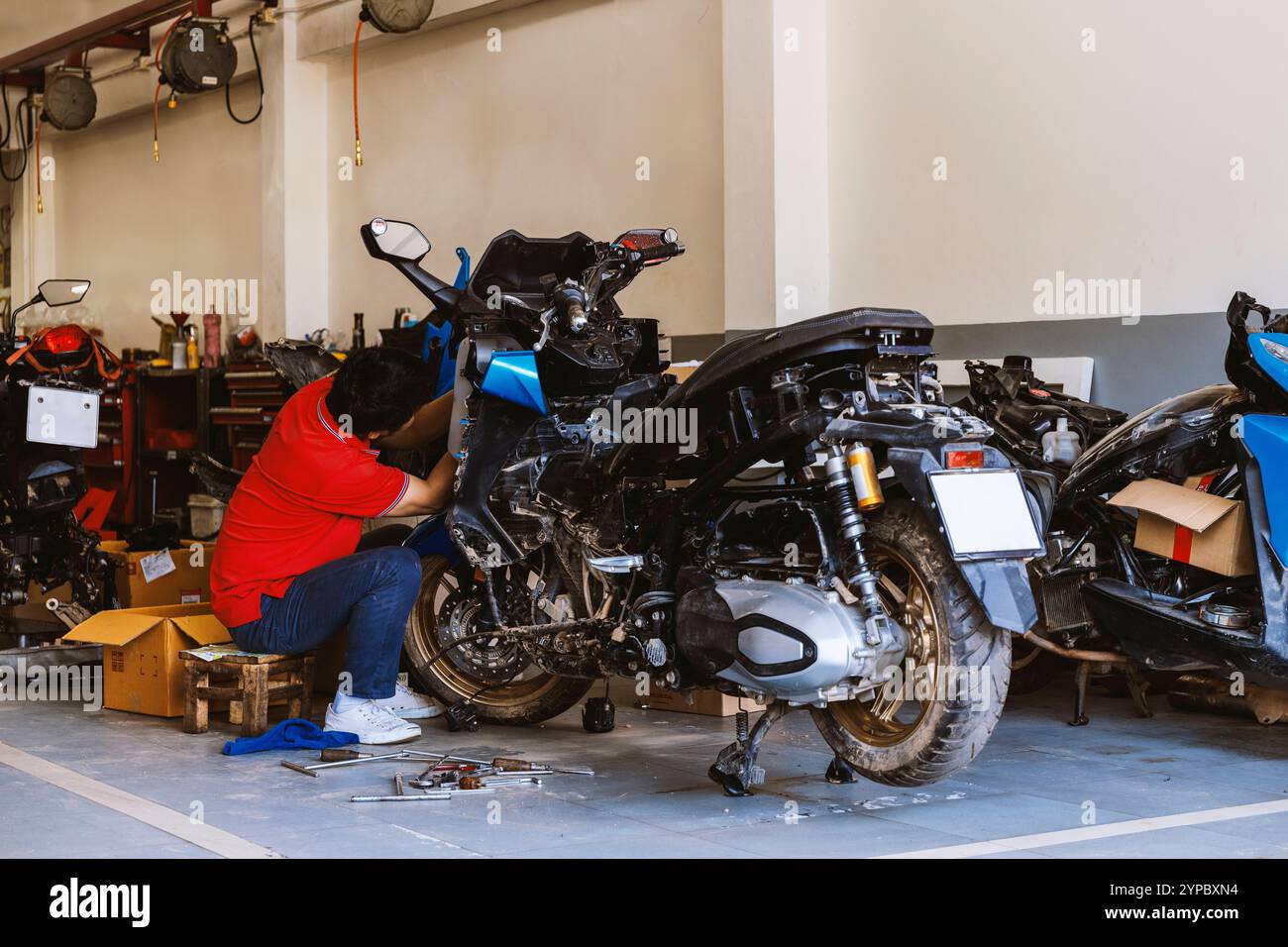 mécanicien qualifié réparant une moto dans un atelier, entouré d'outils et de pièces de rechange, capturant l'essence du travail d'entretien et de réparation Banque D'Images