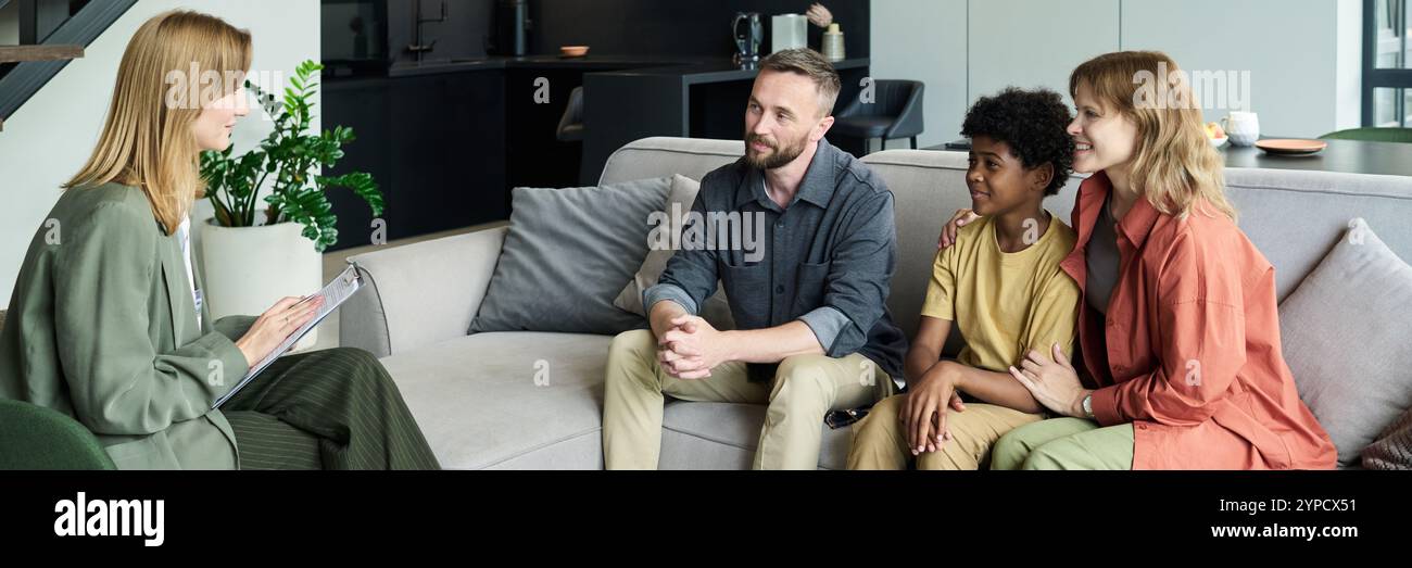 Famille souriante assis sur le canapé pendant la séance de conseil, engager une conversation avec le thérapeute tenant une planche à pince dans le salon moderne rempli de lumière naturelle Banque D'Images