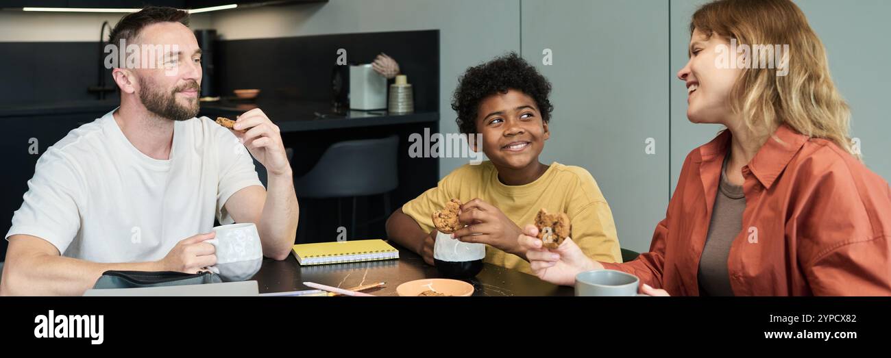 Enfant et deux adultes prenant le petit déjeuner ensemble dans un cadre de cuisine moderne, s'engageant dans une conversation animée tout en partageant nourriture et boissons Banque D'Images