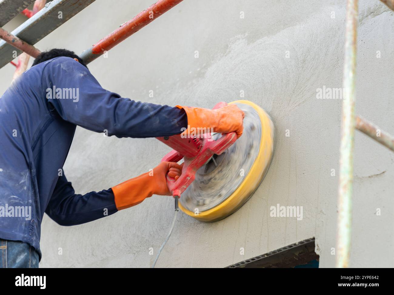 Le travailleur utilise le mortier de machine de polissage électrique sur le mur dans le chantier de construction. Banque D'Images