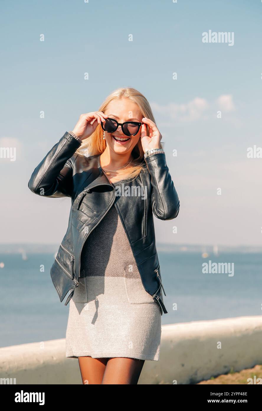 Jeune femme joyeuse ajustant ses lunettes de soleil tout en profitant d'une journée ensoleillée au bord de la mer Banque D'Images