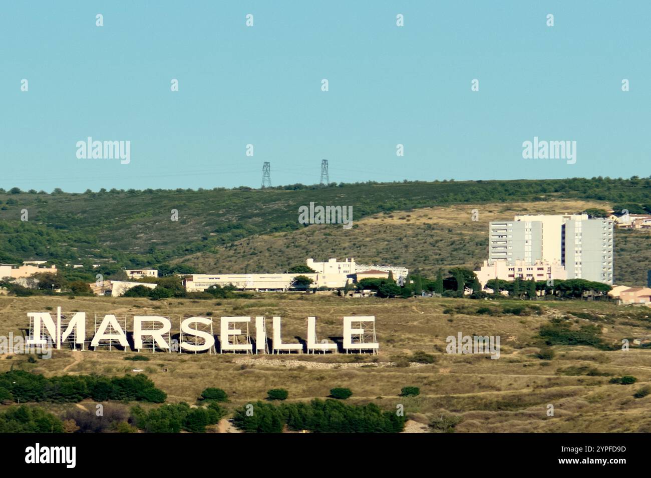 Marseille. France - 30 novembre 2024 : Grand panneau marseille sur une colline à proximité d'immeubles et de pylônes électriques Banque D'Images