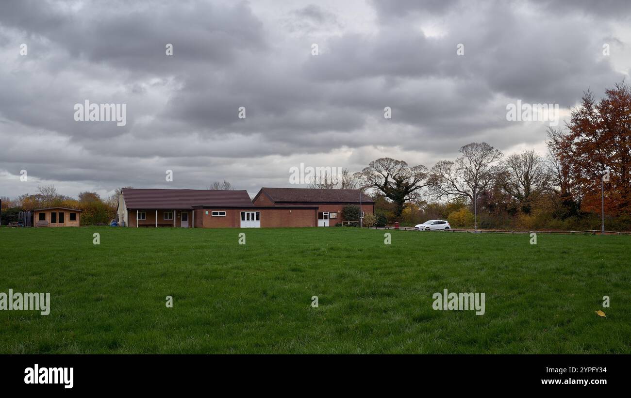 Vue à travers les terrains de jeu d'un club House en brique d'un seul étage sur une journée nuageuse avec une ligne des arbres en arrière-plan Banque D'Images