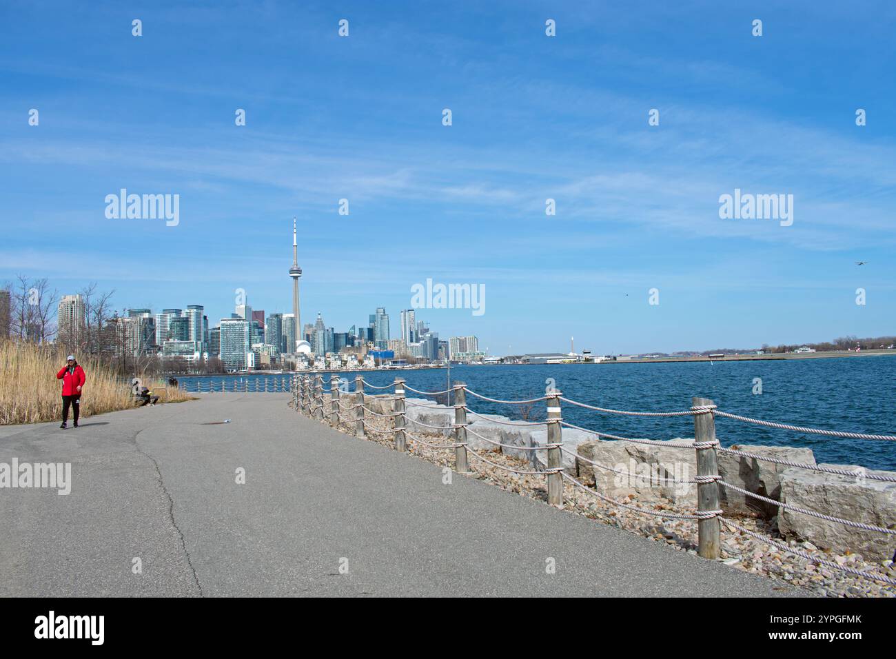 Un homme est assis sur un banc et un homme portant un manteau rouge sur le sentier William G Davis à Trillium Park, Ontario place. Toronto et la Tour CN en arrière-plan. Banque D'Images