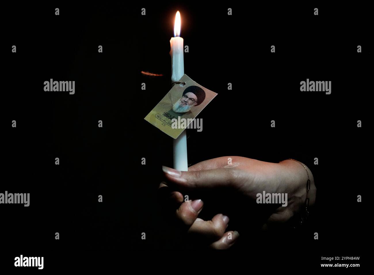 A woman holds a candle with a small portrait of Hezbollah leader Sayyed Hassan Nasrallah, at the site where he was killed by Israeli airstrikes late September during a memorial ceremony in Dahiyeh, in the southern suburb of Beirut, Lebanon, Saturday, Nov. 30, 2024. (AP Photo/Hussein Malla) Banque D'Images