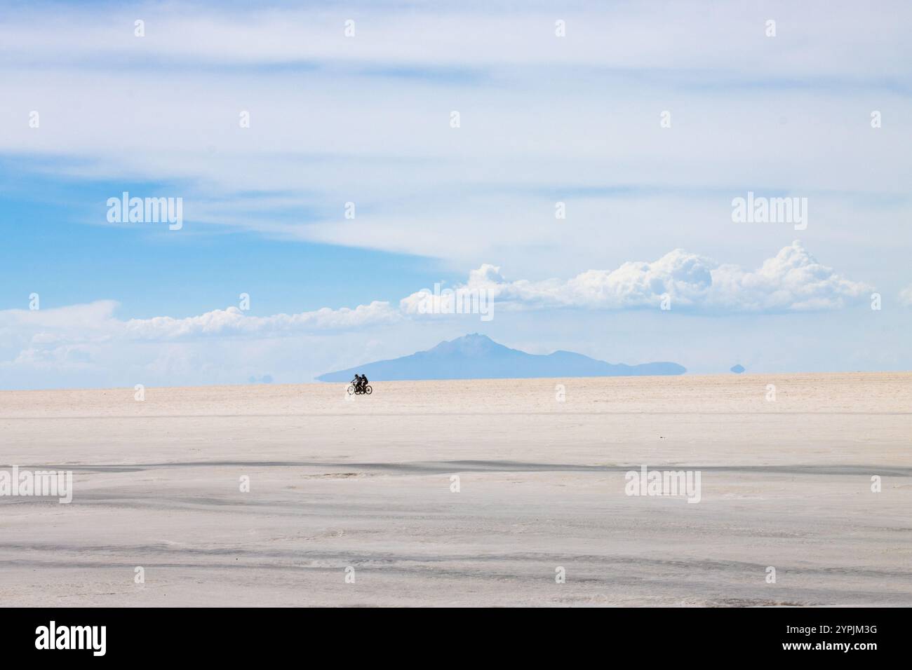 Les gens font du vélo dans les marais de sel blanc immaculé de Salar de Uyuni sous un ciel bleu vif, Bolivie. Banque D'Images