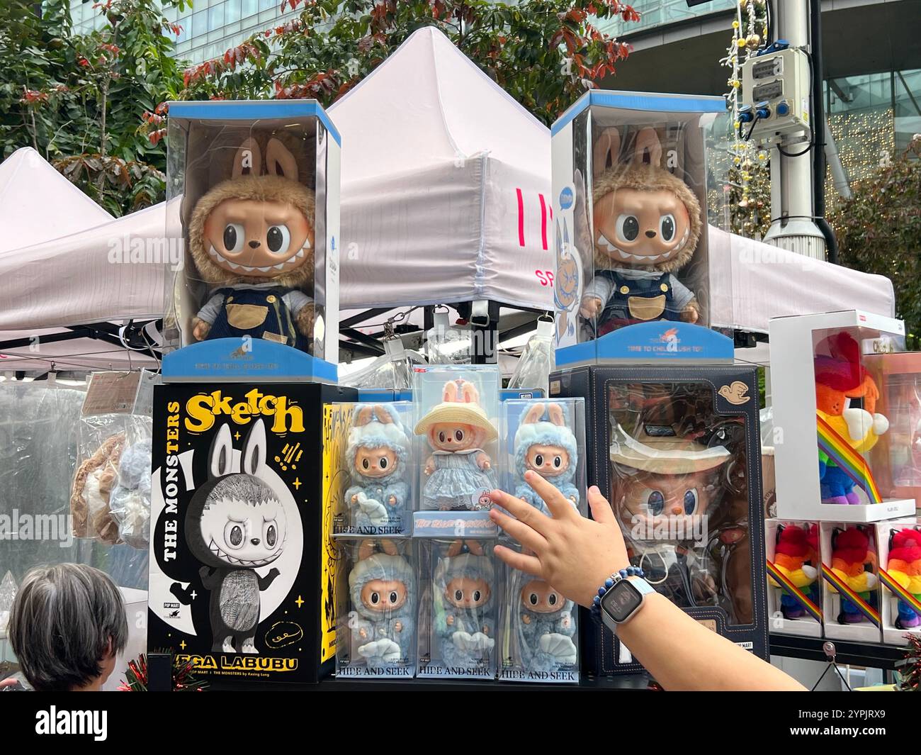 Labubu est un célèbre personnage de jouet en peluche populaire avec un sourire espiègle, des dents tranchantes, un corps rond et fourré. Une main pour atteindre le coffre à jouets. Singapour. Banque D'Images