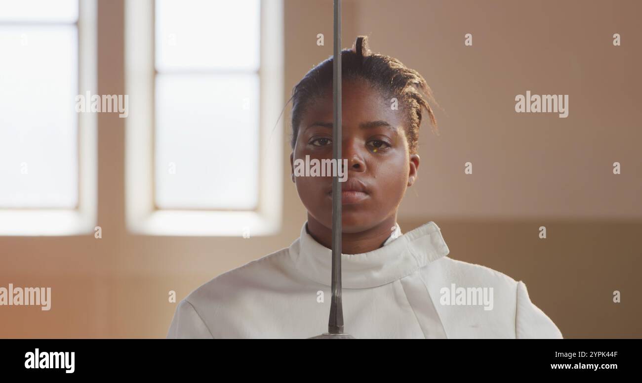 Portrait d'une athlète escrimeuse biraciale confiante au cours d'un entraînement d'escrime dans un gymnase, s Banque D'Images