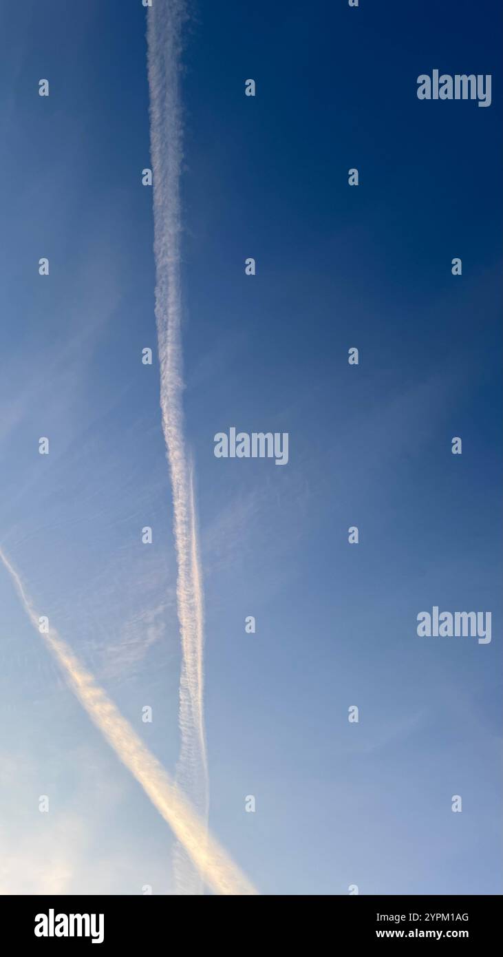 Deux traînées, apparaissant comme de longues traînées blanches, sont bien en évidence contre un ciel bleu clair et pâle. Les traînées présentent de légères variations dans Banque D'Images