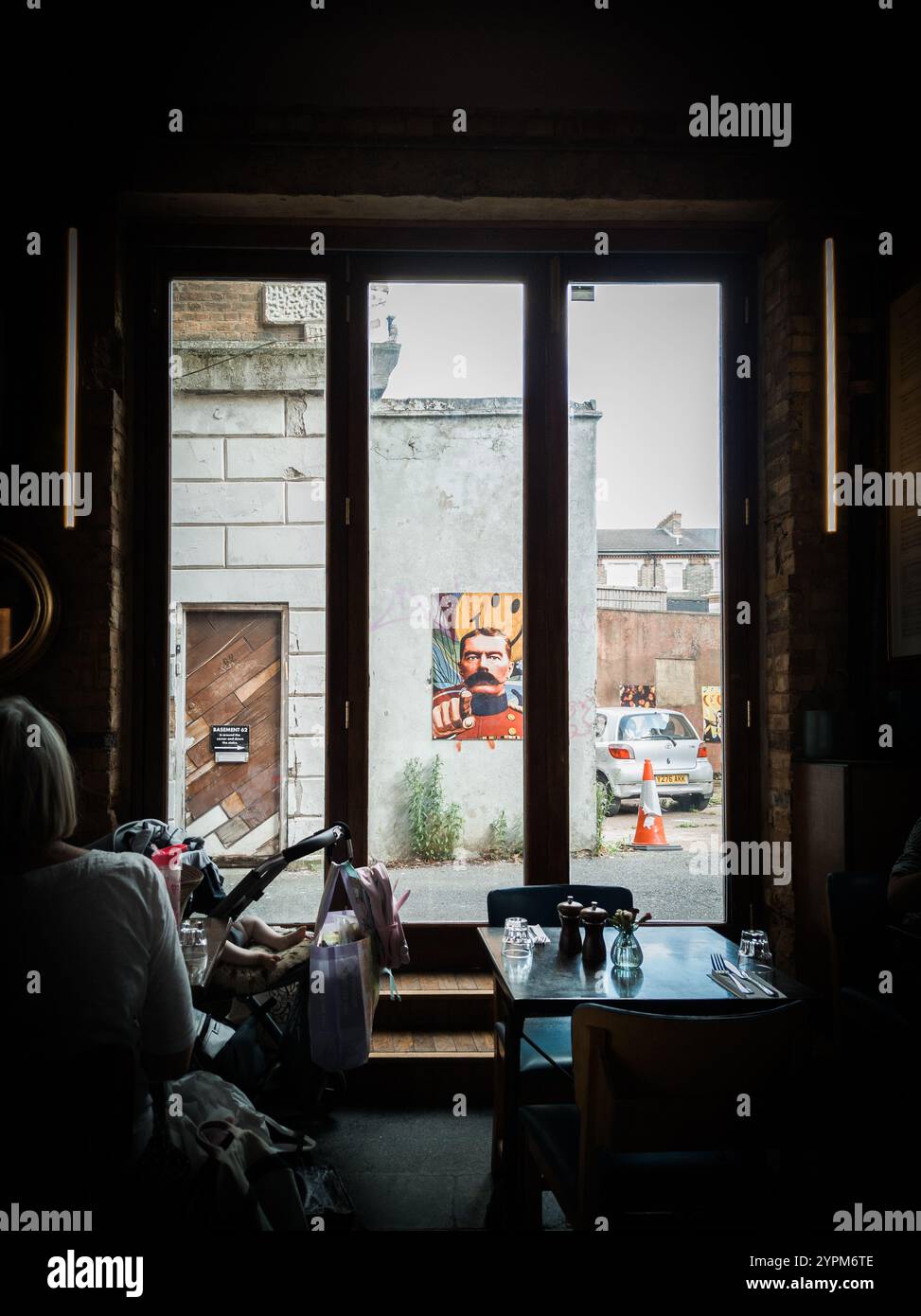 Vue intérieure confortable du café encadrant une murale de rue vibrante à travers de grandes fenêtres à cadre en bois avec un éclairage naturel doux Banque D'Images