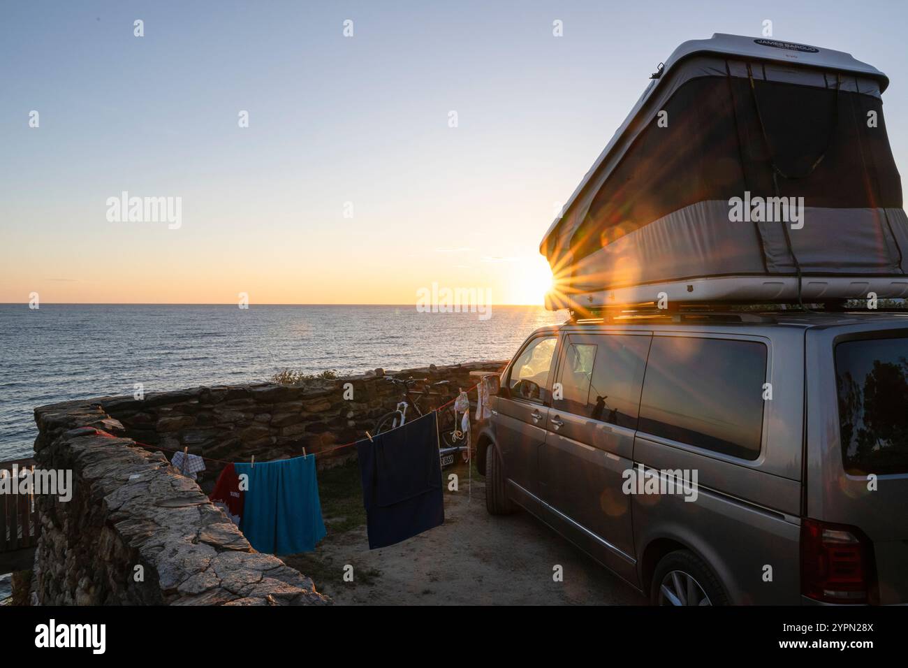 Lever de soleil lumineux derrière un bus VW Multivan Bully avec tente de toit sur la côte près de Collioure, Côte Vermeille, Languedoc-Roussillion, Occitanie, France Banque D'Images