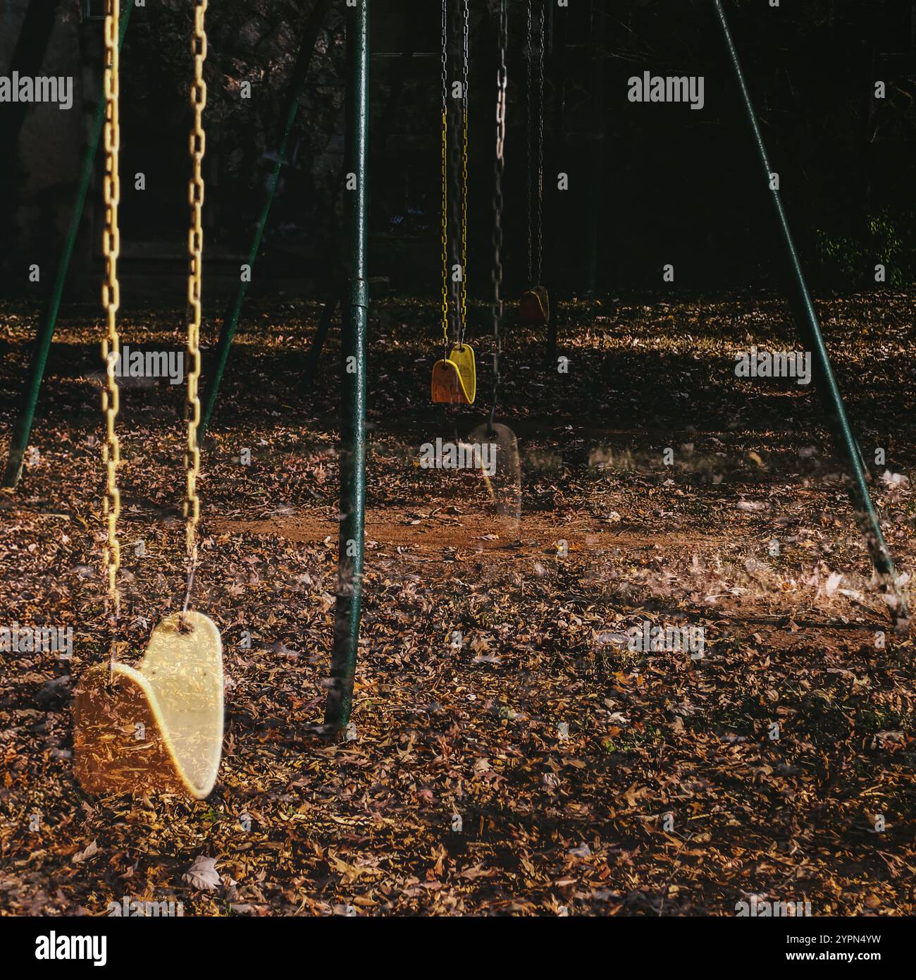 Des balançoires vides pendent encore dans une aire de jeux, entourées de feuilles tombées qui couvrent le sol. Banque D'Images