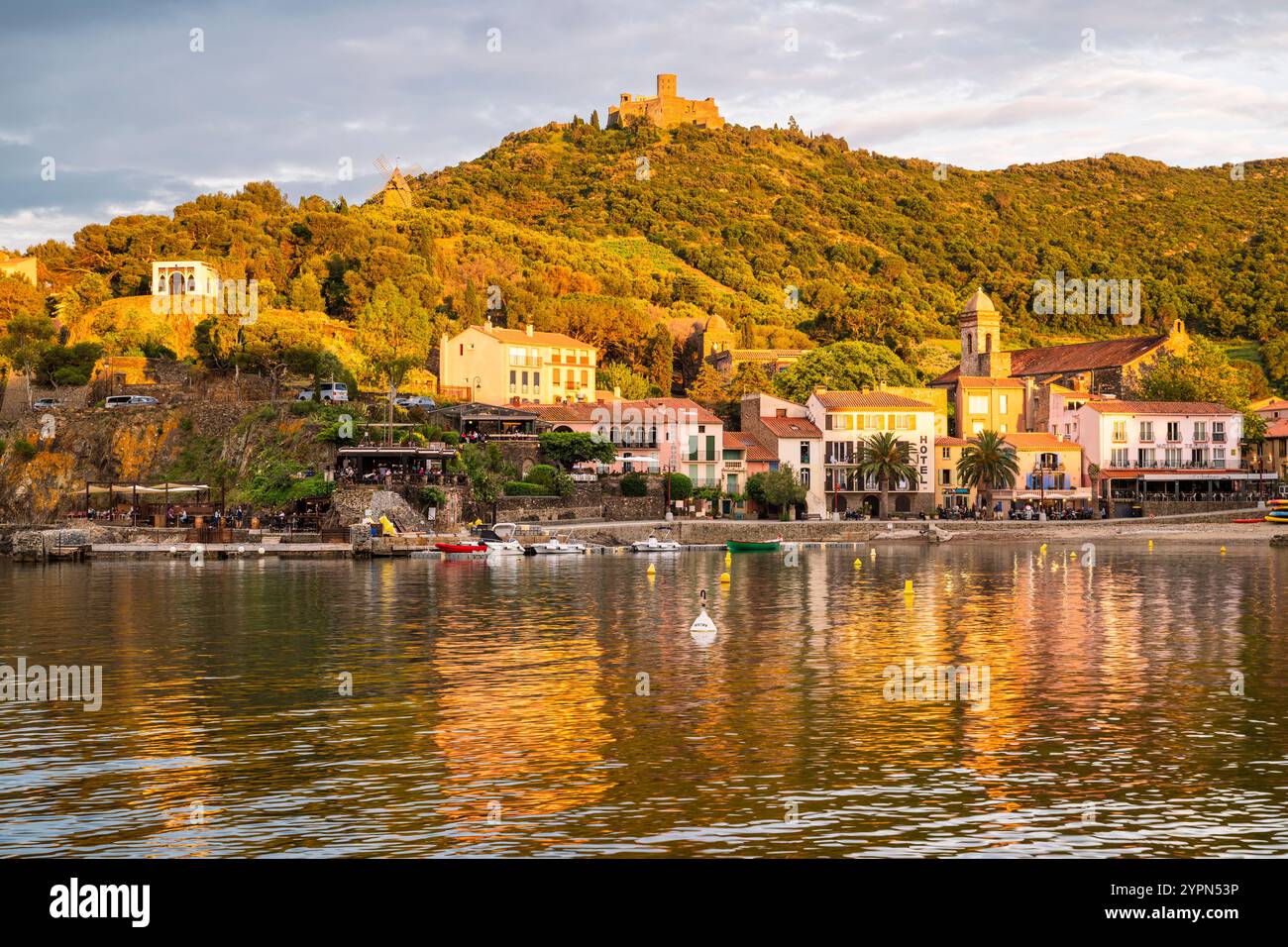Hôtels, bars et restaurants sur la promenade de la plage de Collioure en contrebas du Fort Saint-Elme illuminé par le coucher du soleil, Languedoc-Roussillion, France Banque D'Images