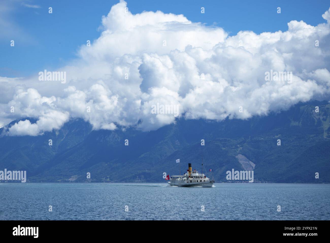 Un bateau à aubes sur le lac Léman glissant au-dessus de l'eau bleue. Situation sur une belle journée d'été avec des montagnes et des formations nuageuses en arrière-plan Banque D'Images