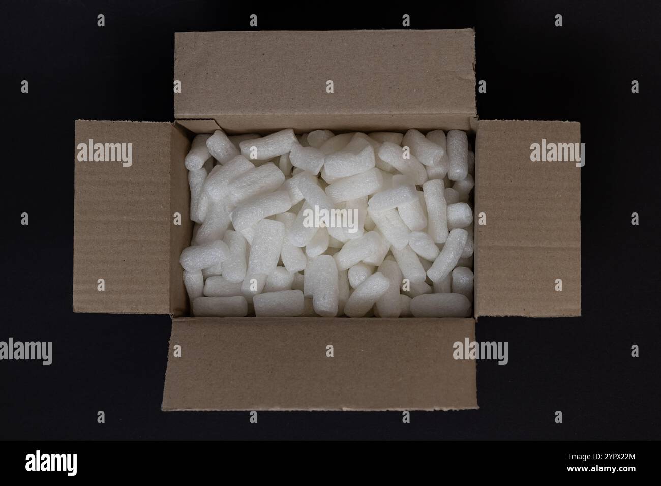 Boîte en carton remplie de polystyrène blanc sur fond noir, conçue pour protéger les objets fragiles pendant le transport Banque D'Images
