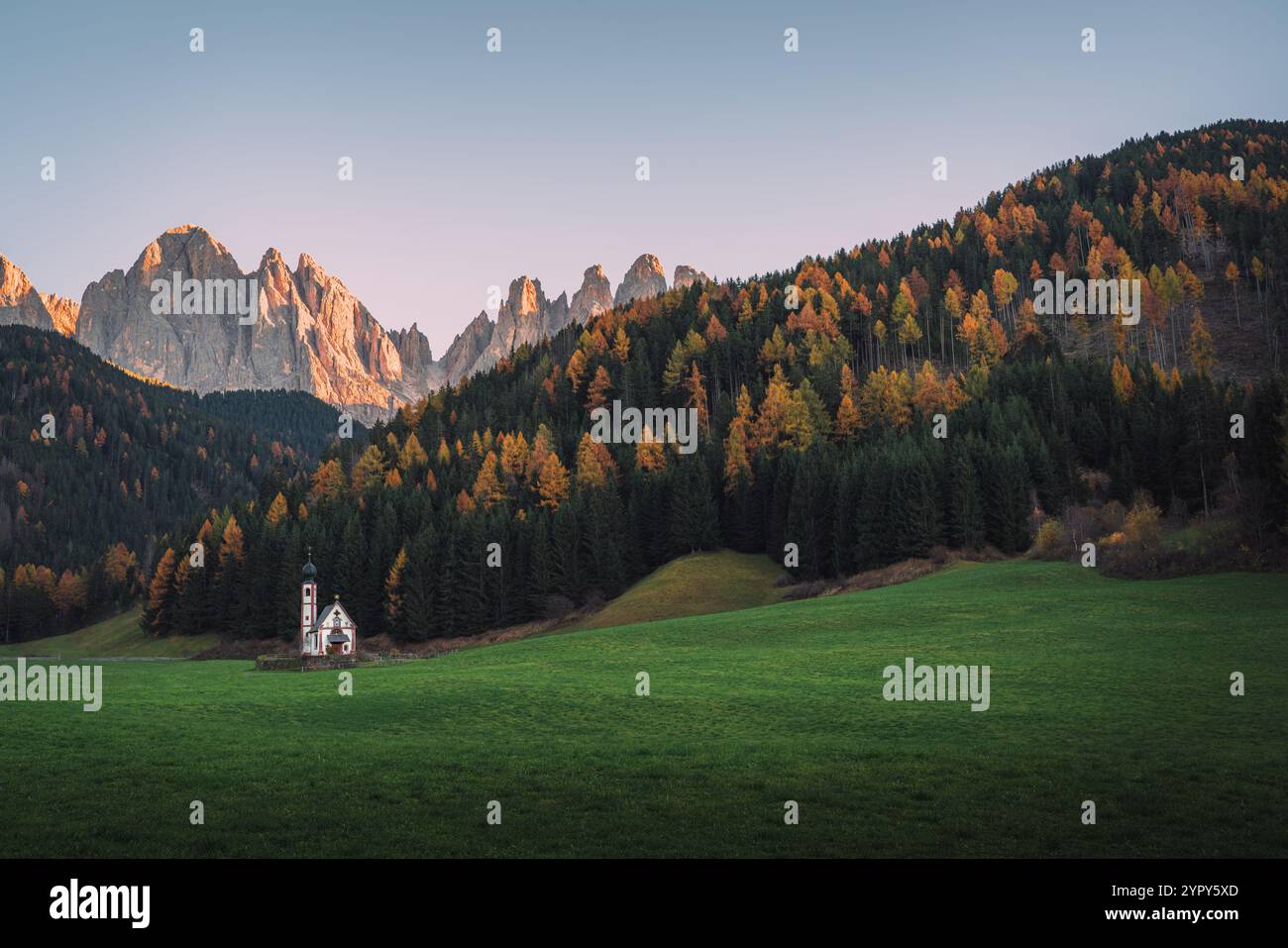 Charmante chapelle alpine dans Mountain Meadow : scène de coucher de soleil sereine entourée de pins et de montagnes dolomitiques, parfaite pour capturer la beauté de la nature Banque D'Images