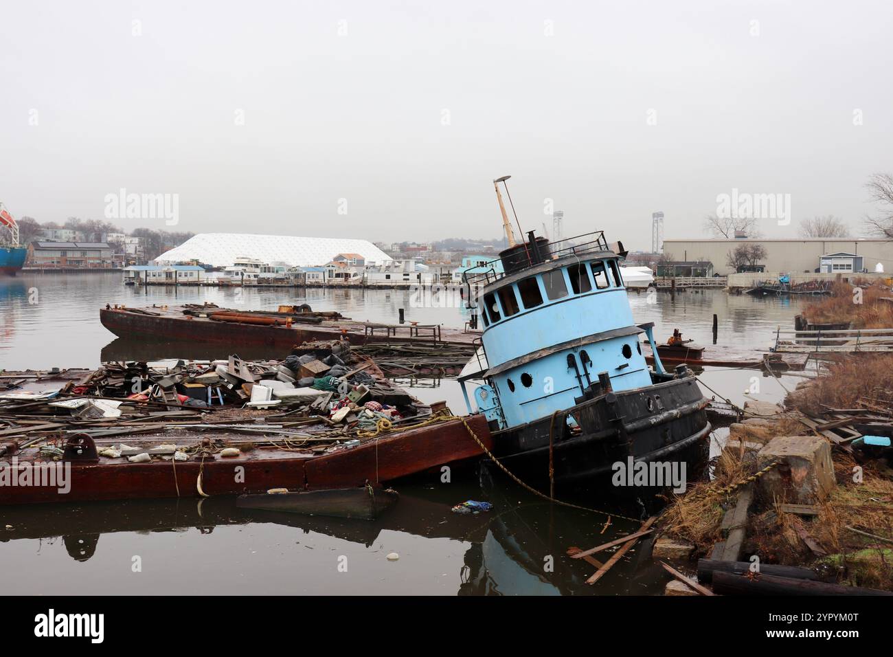 Un remorqueur bleu abandonné amarré à un quai couvert de débris à Chelsea Creek à East Boston, Massachusetts Banque D'Images
