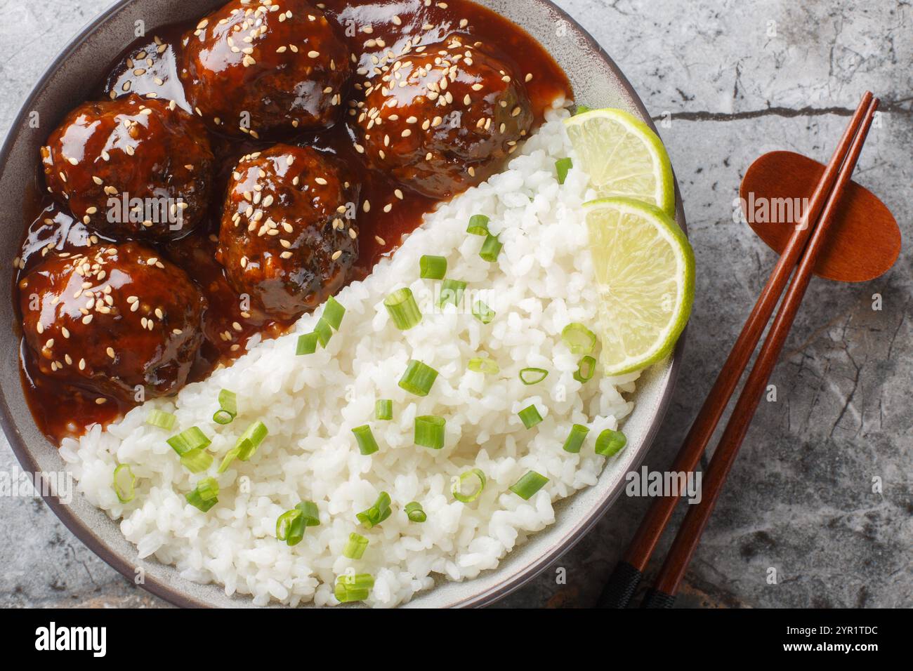 Boulettes de viande asiatiques enrobées de sauce sucrée et épicée à base de sriracha, sauce soja, gingembre, miel et ail servis avec du riz en gros plan sur le bol Banque D'Images
