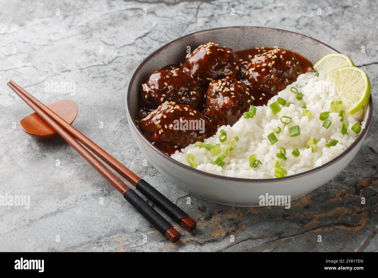 Boulettes de viande chinoises sucrées épicées dans une sauce sriracha au miel servies avec du riz en gros plan dans un bol sur la table. horizontal Banque D'Images