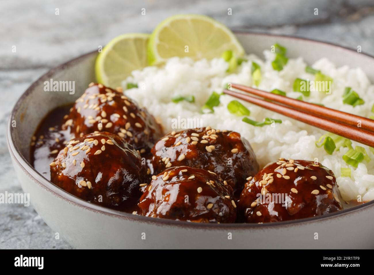Boulettes de viande asiatiques enrobées de sauce sucrée et épicée à base de sriracha, sauce soja, gingembre, miel et ail servis avec du riz en gros plan sur le bol Banque D'Images