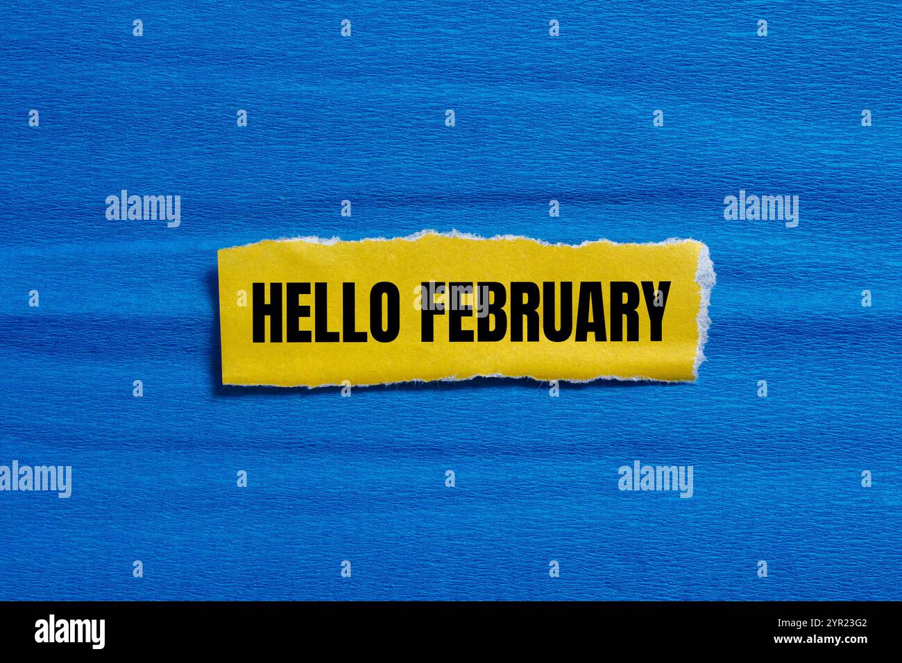 Bonjour février message écrit sur un morceau de papier jaune déchiré déchiré avec fond bleu. Symbole conceptuel bonjour février. Copier l'espace. Banque D'Images