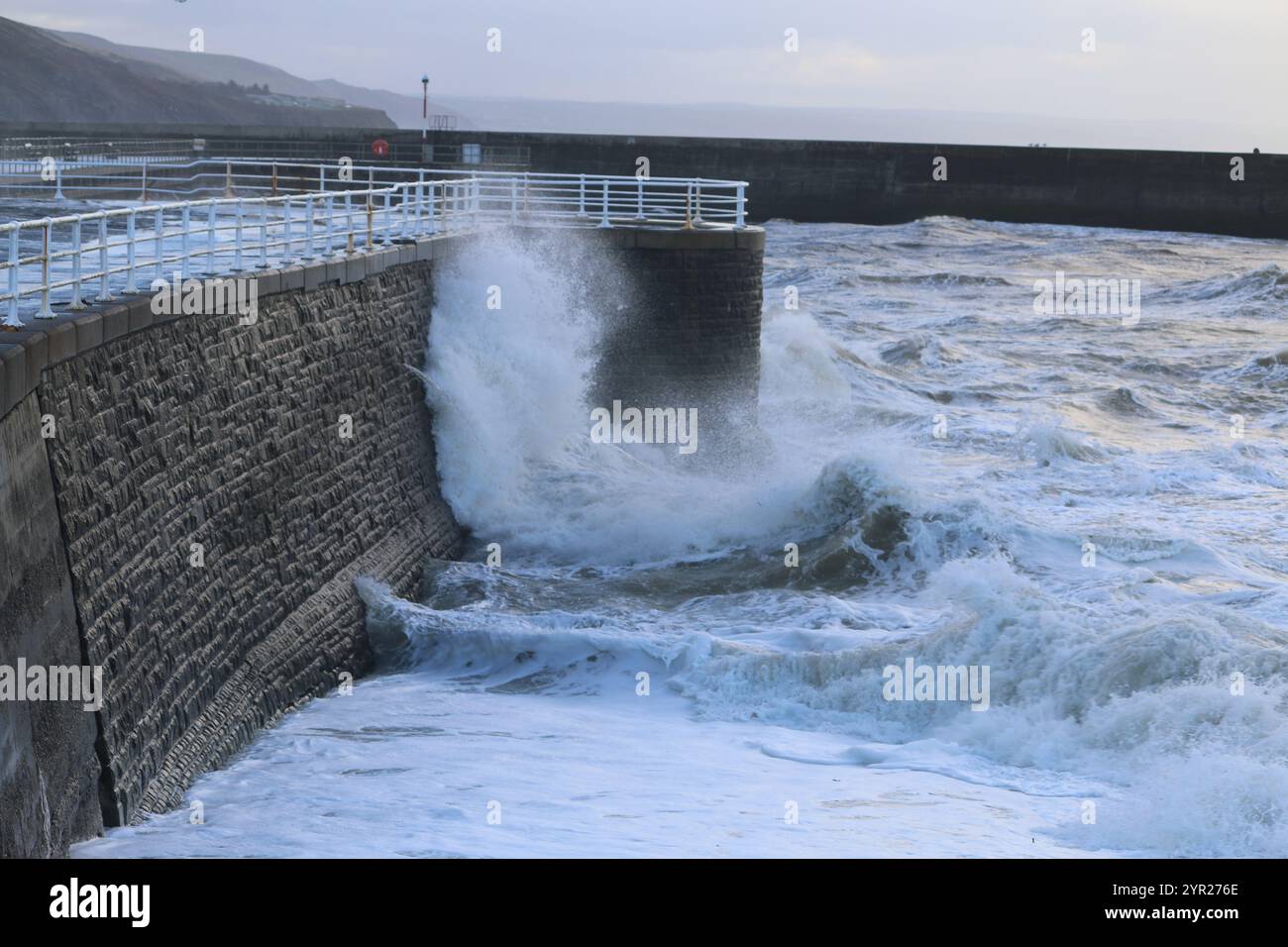 Aberystwyth Wales UK Météo 2 décembre 2024. Un matin d'hiver froid et bruyant autour de la côte galloise, de grandes vagues s'écrasent sur les défenses maritimes et la lumière du port avec un ciel rose au-dessus de la tête, crédit : mike davies/Alamy Live News Banque D'Images