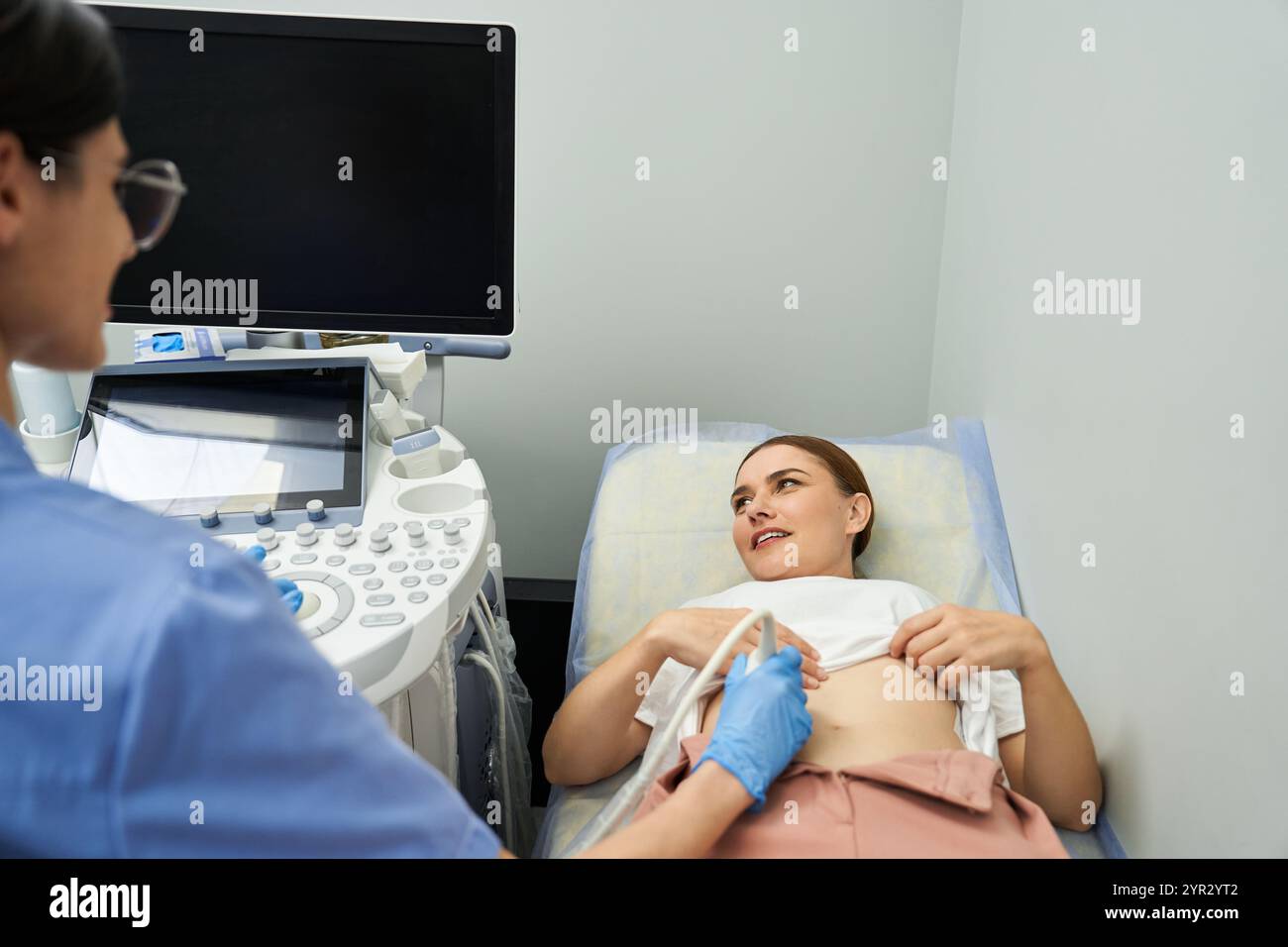 Un gynécologue portant une blouse de laboratoire effectue une échographie sur une patiente dans un environnement de soins de santé. Banque D'Images